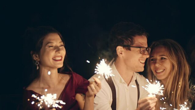 Large group of multiracial friends or acquaintances holding and waving sparklers. Hipster guys celebrating holiday. Cheerful, happy group of people enjoying time together at party. Lifestyle concept.