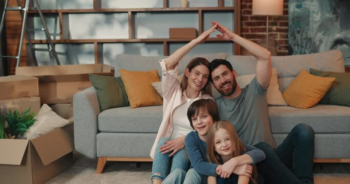 Cheerful maaried man and woman making roof with hands, while sitting with children and enjoying new spacious apartment 