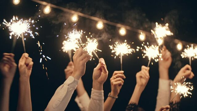 Close-up of hands or palms holding and waving burning sparklers in front of black or dark background. Sparkling lights at birthday party, wedding, Party Party, Party Party, Party.