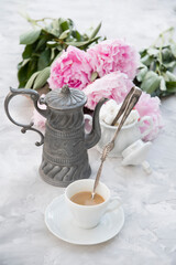 vintage still life with a cup of coffee against a bouquet of pink peonies 