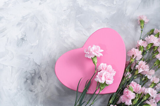 pink carnations and a heart-shaped box on a light gray cement background, a gift