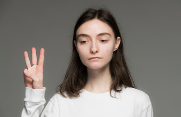close-up portrait of a young Ukrainian girl who shows the number with her hands on a gray background