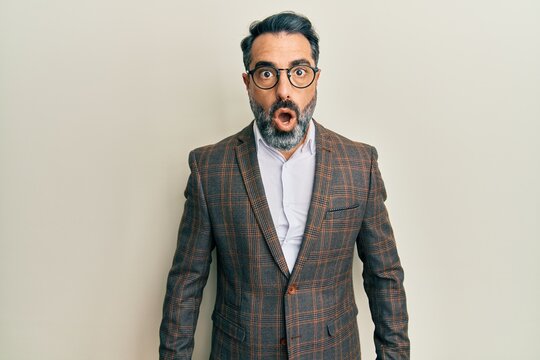 Middle age man with beard and grey hair wearing business jacket and glasses afraid and shocked with surprise expression, fear and excited face.