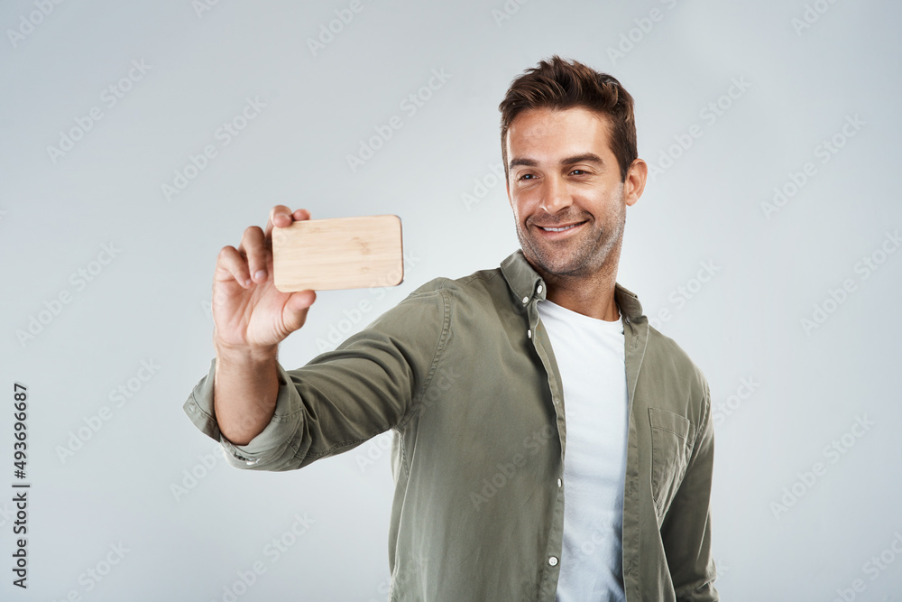 Poster selfie time. studio shot of a cheerful young man taking a self portrait with his cellphone while sta