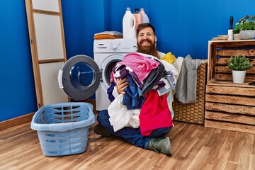 Redhead man with long beard putting dirty laundry into washing machine smiling with a happy and cool smile on face. showing teeth.