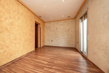 Empty living room with chestnut wood floors and freshly painted walls with draping technique and exit to a terrace with aluminum doors