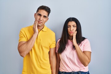 Naklejka premium Young couple standing over isolated background touching mouth with hand with painful expression because of toothache or dental illness on teeth. dentist