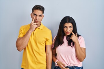Fototapeta premium Young couple standing over isolated background pointing to the eye watching you gesture, suspicious expression