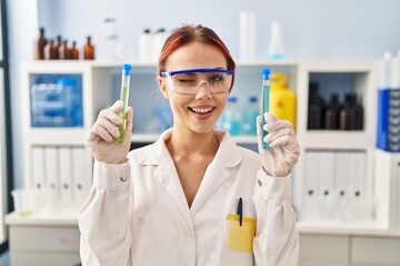 Young caucasian woman working at scientist laboratory holding samples winking looking at the camera...