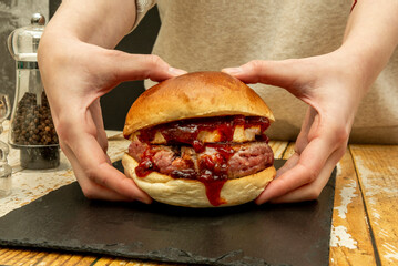Delicious beef burger with goat cheese and lots of spicy tomato jam held in two hands on a black...