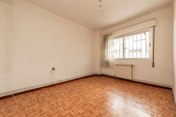 empty room with similar wood sintasol floors, aluminum window with bars and white aluminum radiators