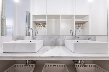 Bathroom decorated with twin porcelain sinks on white marble countertops and white painted wicker baskets