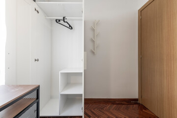 Open white wardrobe with shelving, clothes rail and black hangers