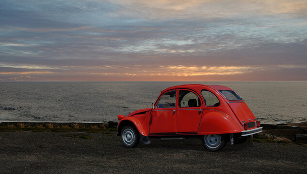 Carro antigo da marca Citroen modelo 2Cv vermelho estacionado á beira mar ao fim da tarde com por do sol 
