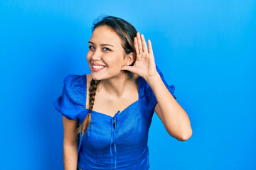 Young hispanic girl wearing casual clothes smiling with hand over ear listening an hearing to rumor or gossip. deafness concept.