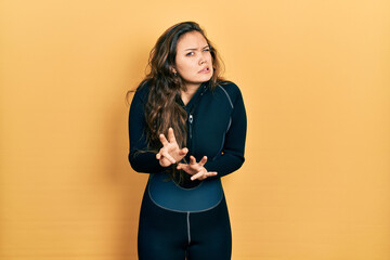 Young hispanic girl wearing diver neoprene uniform disgusted expression, displeased and fearful doing disgust face because aversion reaction.