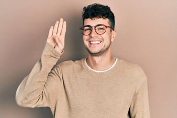 Young hispanic man wearing casual clothes and glasses waiving saying hello happy and smiling, friendly welcome gesture