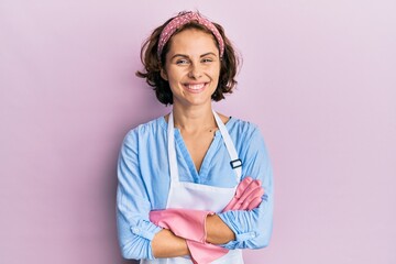 Young brunette woman wearing cleaner apron and gloves happy face smiling with crossed arms looking at the camera. positive person. - obrazy, fototapety, plakaty