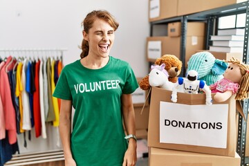 Beautiful caucasian woman wearing volunteer t shirt at donations stand winking looking at the...