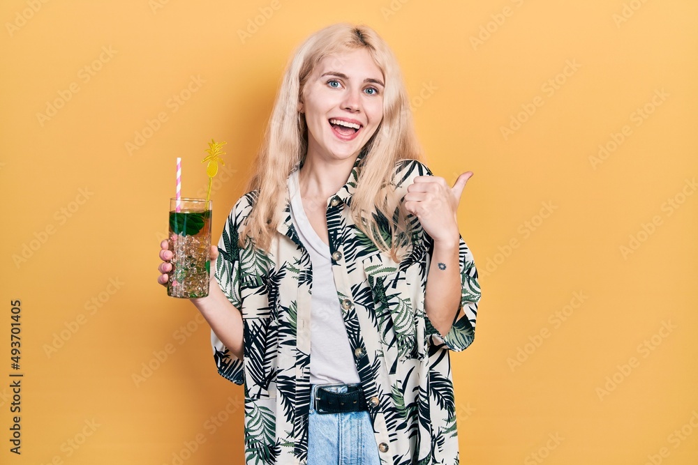 Sticker Beautiful caucasian woman with blond hair drinking mojito glass pointing thumb up to the side smiling happy with open mouth