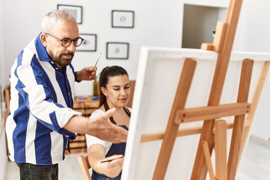 Senior painting teacher man teaching art to young woman painting on canvas at art studio