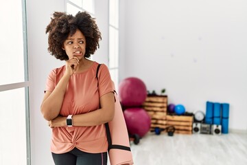 African american woman with afro hair holding yoga mat at pilates room thinking worried about a question, concerned and nervous with hand on chin