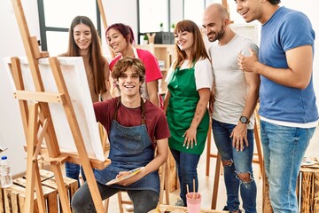 Group of young paint students smiling happy and looking draw of partner at art studio.