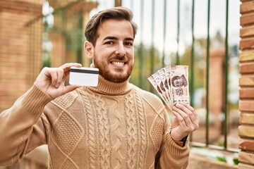 Young caucasian man holding mexican pesos banknotes and credit card at the city.