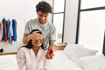 Young latin couple on marriage proposal holding engagement ring at the bedroom.