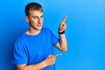 Young caucasian man wearing casual blue t shirt smiling and looking at the camera pointing with two hands and fingers to the side.
