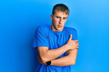 Naklejka premium Young caucasian man wearing casual blue t shirt shaking and freezing for winter cold with sad and shock expression on face