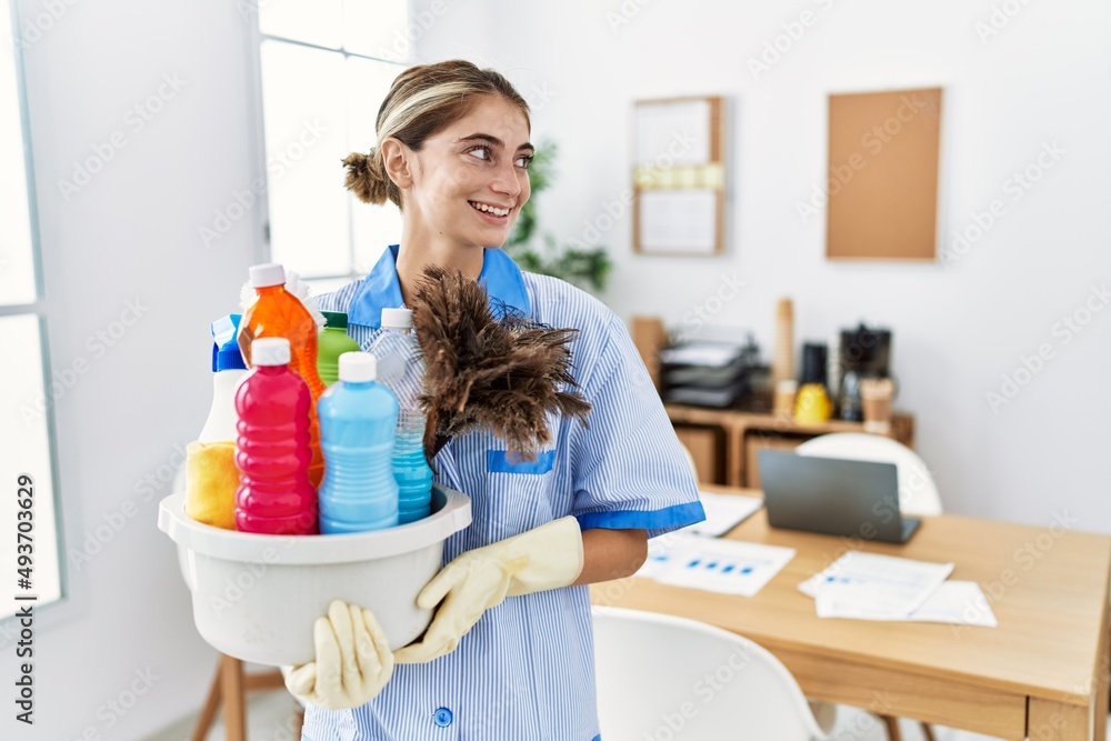 Sticker young blonde woman wearing cleaner uniform holding cleaning products looking away to side with smile