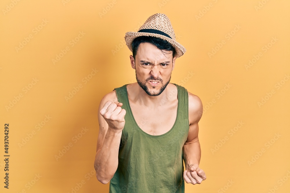 Canvas Prints Young hispanic man wearing summer hat angry and mad raising fist frustrated and furious while shouting with anger. rage and aggressive concept.