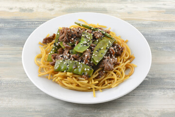Mongolian style beef with snow peas and sesame seeds on noodles on white late