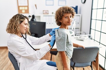 Mother and son wearing doctor uniform auscultating child back at clinic