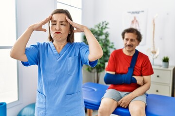 Middle age doctor woman with patient with arm injury at rehabilitation clinic with hand on head, headache because stress. suffering migraine.