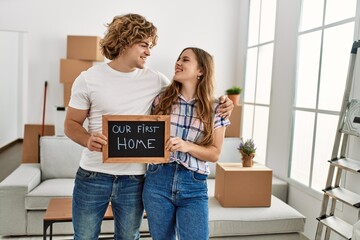 Young caucasian couple holding our new home blackboard hugging each other at new home