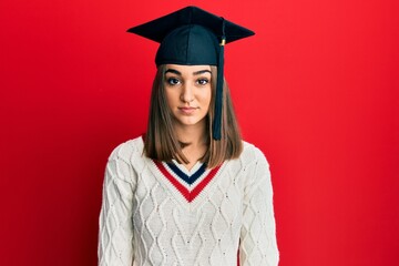 Young brunette girl wearing graduation cap with serious expression on face. simple and natural...