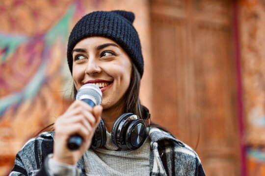 Young hispanic woman smiling happy using headphones and microphone at the city.