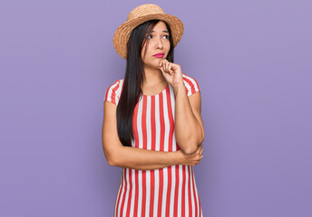 Young hispanic woman wearing summer hat serious face thinking about question with hand on chin,...