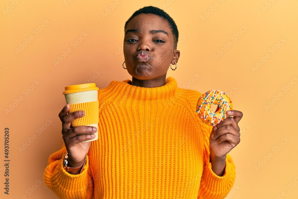 Sticker young african american woman eating doughnut and drinking take away coffee puffing cheeks with funny