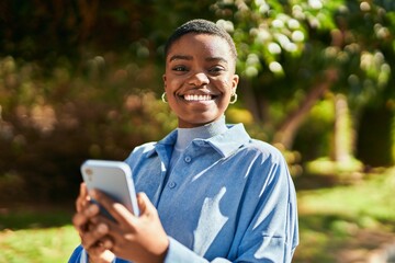 Fototapeta premium Young african american woman smiling happy using smartphone at the city