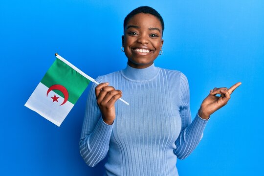 Young african american woman holding algeria flag smiling happy pointing with hand and finger to the side