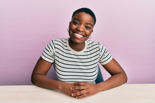 Young african american woman wearing casual clothes sitting on the table with a happy and cool smile on face. lucky person.