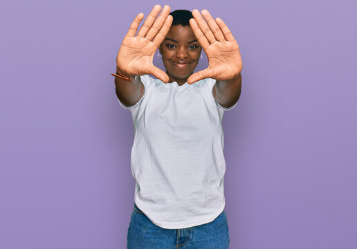 Young african american woman wearing casual white t shirt doing frame using hands palms and fingers, camera perspective