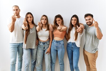 Group of young friends standing together over isolated background showing middle finger, impolite...