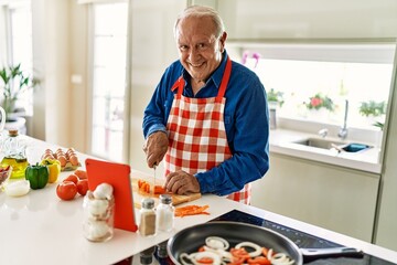 Senior man smiling confident cooking and watching online recipe at kitchen