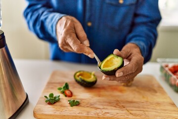 Obraz na płótnie Canvas Senior man cutting avocado at kitchen