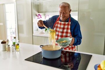 Senior man smiling confident cooking spaghetti at kitchen