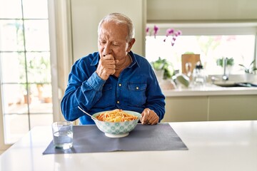 Senior man with grey hair eating pasta spaghetti at home feeling unwell and coughing as symptom for cold or bronchitis. health care concept.